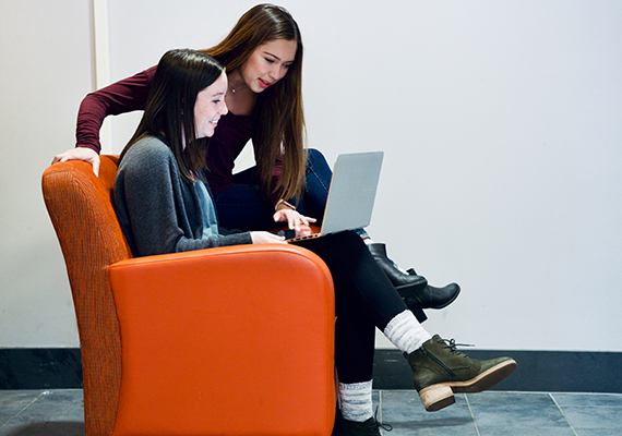 Two female students work on a project together with a laptop computer.